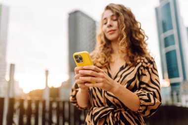 Bir metropolün arka planına telefon tutan genç bir kadının ellerinin yakın çekimi. Güzel bir kadın telefonda mesaj atıyor ve dışarıda gezmekten zevk alıyor. Teknoloji kavramı, şehirler.