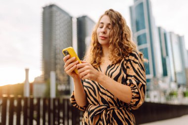 Bir metropolün arka planına telefon tutan genç bir kadının ellerinin yakın çekimi. Güzel bir kadın telefonda mesaj atıyor ve dışarıda gezmekten zevk alıyor. Teknoloji kavramı, şehirler.