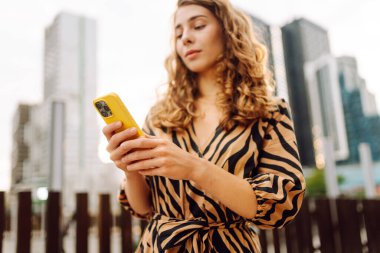 Bir metropolün arka planına telefon tutan genç bir kadının ellerinin yakın çekimi. Güzel bir kadın telefonda mesaj atıyor ve dışarıda gezmekten zevk alıyor. Teknoloji kavramı, şehirler.