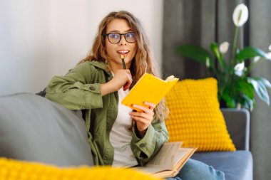 Sarı defterli gülümseyen kadının portresi rahat bir odada koltukta oturuyor. Genç kız öğrenci evdeki oturma odasında ders çalışıyor. Eğitim, dinlenme ve rahatlık kavramı.