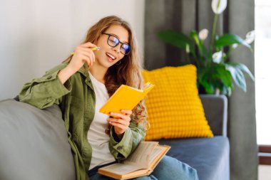 Sarı defterli gülümseyen kadının portresi rahat bir odada koltukta oturuyor. Genç kız öğrenci evdeki oturma odasında ders çalışıyor. Eğitim, dinlenme ve rahatlık kavramı.