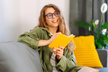 Sarı defterli gülümseyen kadının portresi rahat bir odada koltukta oturuyor. Genç kız öğrenci evdeki oturma odasında ders çalışıyor. Eğitim, dinlenme ve rahatlık kavramı.