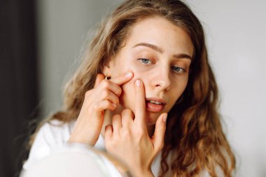 Güzel bir kadının portresi tenine dokunuyor ve cildindeki kızarıklığı inceliyor. Genç kadın aynadaki yansımasına bakıyor. Kozmetik ve güzellik konsepti. Dermatoloji.