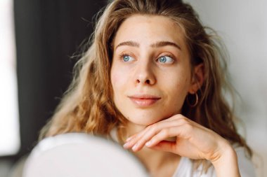 Güzel bir kadının portresi tenine dokunuyor ve cildindeki kızarıklığı inceliyor. Genç kadın aynadaki yansımasına bakıyor. Kozmetik ve güzellik konsepti. Dermatoloji.