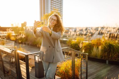 Güzel bir kadın gün batımından zevk alır ve telefonuyla selfie çeker. Şık bir iş kadını blogu ya da çatıdaki video konferansları şehrin hareketliliğinin tadını çıkarıyor. Blog yazma, boş zaman kavramı.