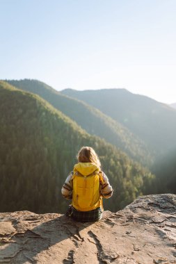 Güzel kadın yürüyüşçü özgürlüğü hissediyor kayalık çıkıntıda durup dağlarda günbatımının tadını çıkarıyor. Genç bayan yürüyüşçü uçurumdaki dağ manzarasına bakıyor. Yürüyüş, macera ve doğa konsepti.