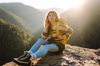 Güzel kadın yürüyüşçü özgürlüğü hissediyor kayalık çıkıntıda durup dağlarda günbatımının tadını çıkarıyor. Genç bayan yürüyüşçü uçurumdaki dağ manzarasına bakıyor. Yürüyüş, macera ve doğa konsepti.