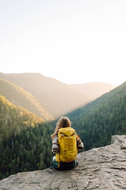 Güzel kadın yürüyüşçü özgürlüğü hissediyor kayalık çıkıntıda durup dağlarda günbatımının tadını çıkarıyor. Genç bayan yürüyüşçü uçurumdaki dağ manzarasına bakıyor. Yürüyüş, macera ve doğa konsepti.