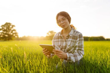 Dijital tabletli bir kadın çiftçinin portresi tarım alanındaki mahsulleri kontrol ediyor. Dışarıda çalışan genç bir tarımcı kadın. Teknoloji ve tarım kavramı.