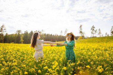 Sarı kolza tohumu tarlasında eğlenen iki genç bayan arkadaş, yürüyüş yapıyorlar. Güzel kadınlar çiçek açan bir alanda birlikte vakit geçiriyorlar. Arkadaşlık, eğlence ve macera kavramı.