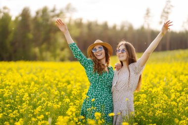 Sarı kolza tohumu tarlasında eğlenen iki genç bayan arkadaş, yürüyüş yapıyorlar. Güzel kadınlar çiçek açan bir alanda birlikte vakit geçiriyorlar. Arkadaşlık, eğlence ve macera kavramı.