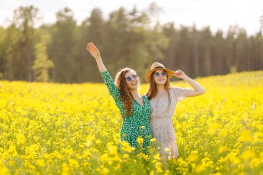 Sarı kolza tohumu tarlasında eğlenen iki genç bayan arkadaş, yürüyüş yapıyorlar. Güzel kadınlar çiçek açan bir alanda birlikte vakit geçiriyorlar. Arkadaşlık, eğlence ve macera kavramı.