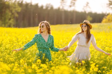 Sarı kolza tohumu tarlasında eğlenen iki genç bayan arkadaş, yürüyüş yapıyorlar. Güzel kadınlar çiçek açan bir alanda birlikte vakit geçiriyorlar. Arkadaşlık, eğlence ve macera kavramı.
