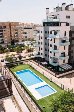 Valencia, İspanya - 20 Haziran 2025: Yüzme havuzu ve bahçe manzaralı modern apartman, güneşli bir yerleşim bölgesinde kentsel yaşam ve eğlence alanı sergileniyor