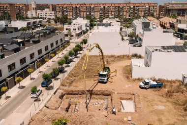 Valencia, İspanya - 20 Haziran 2025: İnşaat sahasında modern evler ve yeşillik ile kentsel alanda temel döken beton pompa kamyonu yer alıyor