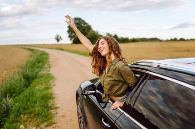 Zevk ve özgürlük hisseden genç bir kadın arabanın camından sarkıyor. Yolculukta olan güzel bir kadın dışarıda eğleniyor. Yol macerası ve tatil konsepti.