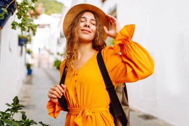 Beyaz evlere karşı poz veren parlak elbiseli güzel bir turist. Genç kadın macerada özgürlük ve haz hissediyor. Seyahat ve hafta sonu konsepti.