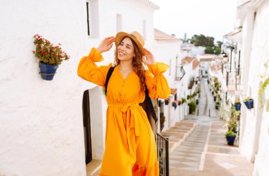 Beyaz evlere karşı poz veren parlak elbiseli güzel bir turist. Genç kadın macerada özgürlük ve haz hissediyor. Seyahat ve hafta sonu konsepti.