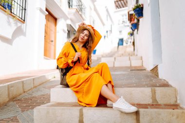 Beyaz evlere karşı poz veren parlak elbiseli güzel bir turist. Genç kadın macerada özgürlük ve haz hissediyor. Seyahat ve hafta sonu konsepti.