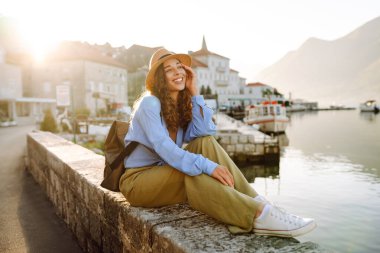 Deniz kenarında şapka takmış genç bir turist, güneşin doğuşunu seyrediyor. Güzel bir kadın özgürlüğü hisseder, dağ manzaralı bir macera arar. Turizm, keyif konsepti.