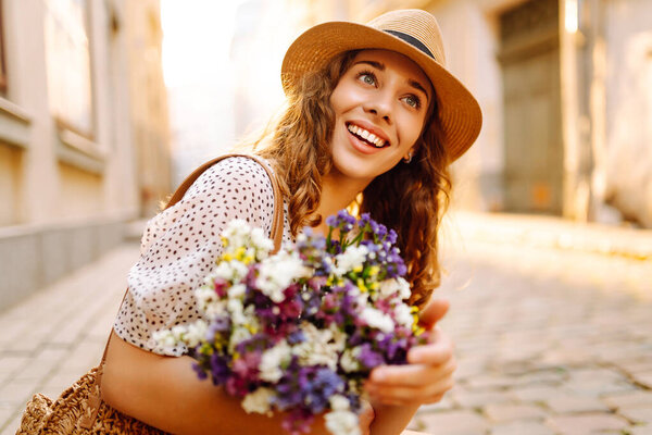 Улыбающаяся женщина с ярким букетом диких цветов наслаждается закатом на улице. Молодая туристка ходит по европейским улицам. Мбаппе, концепция отдыха.