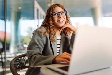 Bir kafedeki verandada dizüstü bilgisayarla çalışan gözlüklü genç bir kadının yakın çekimi. Gülümseyen ve dışarıda çalışmaktan hoşlanan güzel bir iş kadını. İş, teknoloji ve eğlence kavramı.