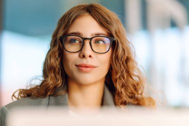 Bir kafedeki verandada dizüstü bilgisayarla çalışan gözlüklü genç bir kadının yakın çekimi. Gülümseyen ve dışarıda çalışmaktan hoşlanan güzel bir iş kadını. İş, teknoloji ve eğlence kavramı.