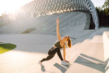 Spor yapan bir kadın gün batımında dışarıda egzersiz yapıyor. Spor giyimli güzel bir kadın spor sahasında antrenman yapıyor. Spor konsepti. Etkin yaşam biçimi.