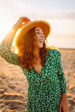 Şapkalı mutlu kadın gün batımını seyrediyor. Gün batımında sahilde duruyor. Genç bayan hava ve deniz manzarasının tadını çıkarıyor. Zevk ve özgürlük kavramı.