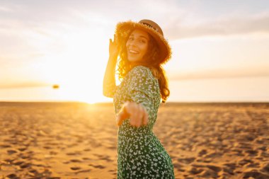 Şapkalı mutlu kadın gün batımını seyrediyor. Gün batımında sahilde duruyor. Genç bayan hava ve deniz manzarasının tadını çıkarıyor. Zevk ve özgürlük kavramı.