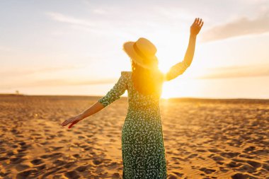 Şapkalı mutlu kadın gün batımını seyrediyor. Gün batımında sahilde duruyor. Genç bayan hava ve deniz manzarasının tadını çıkarıyor. Zevk ve özgürlük kavramı.