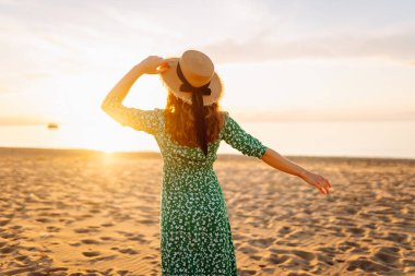 Şapkalı mutlu kadın gün batımını seyrediyor. Gün batımında sahilde duruyor. Genç bayan hava ve deniz manzarasının tadını çıkarıyor. Zevk ve özgürlük kavramı.