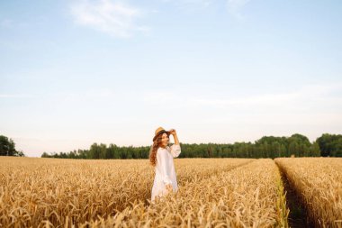 Beyaz elbiseli neşeli kadın altın buğday tarlasında poz veriyor. Genç bayan eğleniyor ve açık havada güneşli havanın tadını çıkarıyor. Doğa ve keyif kavramı.