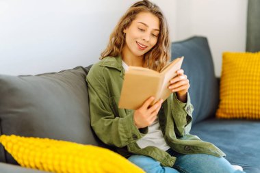 Gözlüklü genç bir kadın rahat bir odada kanepede kitap okumaktan zevk alıyor. Gözlüklü hoş bir kadın kitap okuyor, evde çalışıyor ve dinleniyor. Eğitim, rahatlama ve rahatlama konsepti.