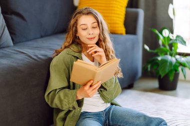 Gözlüklü genç bir kadın rahat bir odada kanepede kitap okumaktan zevk alıyor. Gözlüklü hoş bir kadın kitap okuyor, evde çalışıyor ve dinleniyor. Eğitim, rahatlama ve rahatlama konsepti.