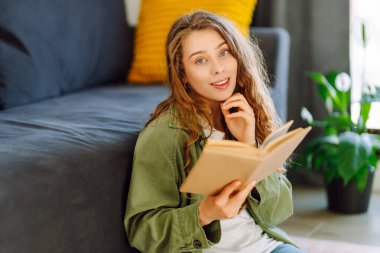 Gözlüklü genç bir kadın rahat bir odada kanepede kitap okumaktan zevk alıyor. Gözlüklü hoş bir kadın kitap okuyor, evde çalışıyor ve dinleniyor. Eğitim, rahatlama ve rahatlama konsepti.