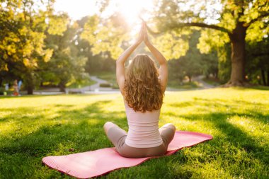 Sunny Park 'ta meditasyon yapan genç bir kadın. Sportif bir kadın, dışarıda yeşil çayır üzerinde egzersiz yapıyor. Rahatlama, spor ve meditasyon konsepti. Etkin yaşam biçimi.