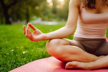 Sunny Park 'ta meditasyon yapan genç bir kadın. Sportif bir kadın, dışarıda yeşil çayır üzerinde egzersiz yapıyor. Rahatlama, spor ve meditasyon konsepti. Etkin yaşam biçimi.