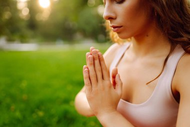 Sunny Park 'ta meditasyon yapan genç bir kadın. Sportif bir kadın, dışarıda yeşil çayır üzerinde egzersiz yapıyor. Rahatlama, spor ve meditasyon konsepti. Etkin yaşam biçimi.