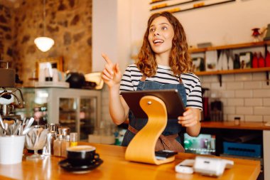 Barın arkasında elinde bir fincan sıcak ve aromatik kahve tutan mutlu bayan barista. Kahve dükkanının genç çalışanı bir müşteriye kahve verir. İçki kavramı, küçük işletmeler..