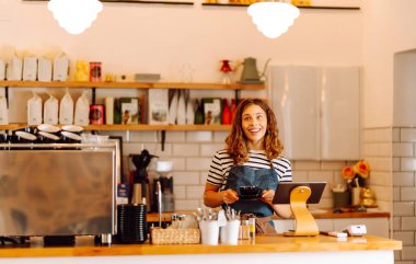 Barın arkasında elinde bir fincan sıcak ve aromatik kahve tutan mutlu bayan barista. Kahve dükkanının genç çalışanı bir müşteriye kahve verir. İçki kavramı, küçük işletmeler..