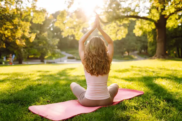 Sunny Park 'ta meditasyon yapan genç bir kadın. Sportif bir kadın, dışarıda yeşil çayır üzerinde egzersiz yapıyor. Rahatlama, spor ve meditasyon konsepti. Etkin yaşam biçimi.