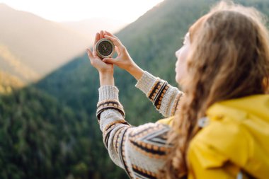 Dağ manzarasına karşı pusula tutan sarı sırt çantalı genç bayan gezginlerin ellerini yakın çekim. Pusulası olan kadın uçurumun kenarında duruyor. Navigasyon, seyahat ve yürüyüş konsepti.