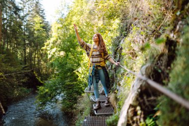 Sırt çantalı gülümseyen bir kadın sık güneşli ormanda kayalık yolda yürüyor. Genç bayan yürüyüşçü dağlık alanda yürüyüş yapıyor. Özgürlük, macera ve doğa kavramı.