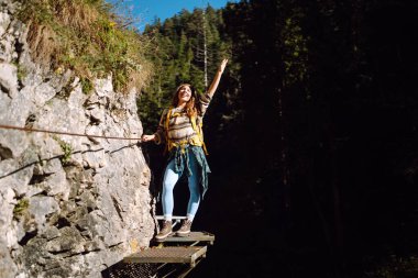 Sırt çantalı gülümseyen bir kadın sık güneşli ormanda kayalık yolda yürüyor. Genç bayan yürüyüşçü dağlık alanda yürüyüş yapıyor. Özgürlük, macera ve doğa kavramı.