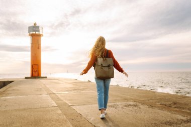 İskelede deniz fenerine hayran güzel bir kadının portresi. Tatlı kadın temiz havada özgürlüğü hissediyor. Özgürlük, doğa konsepti, rahat atmosfer.
