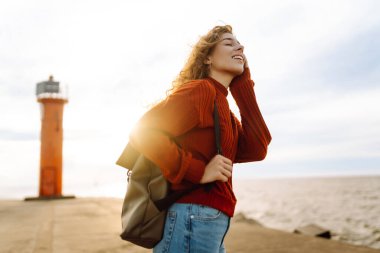 İskelede deniz fenerine hayran güzel bir kadının portresi. Tatlı kadın temiz havada özgürlüğü hissediyor. Özgürlük, doğa konsepti, rahat atmosfer.