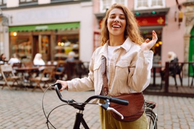 Kıvırcık saçlı genç turist güneşli Avrupa caddelerinde bisiklet sürüyor. Günbatımında günbatımında bir kadın bisikletle gezmekten hoşlanır. Turizm konsepti. Etkin yaşam biçimi.