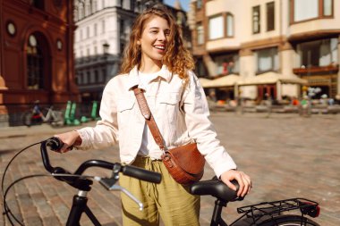 Kıvırcık saçlı genç turist güneşli Avrupa caddelerinde bisiklet sürüyor. Günbatımında günbatımında bir kadın bisikletle gezmekten hoşlanır. Turizm konsepti. Etkin yaşam biçimi.