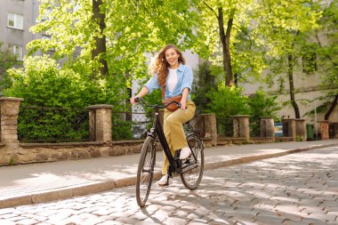 Kıvırcık saçlı genç turist güneşli Avrupa caddelerinde bisiklet sürüyor. Günbatımında günbatımında bir kadın bisikletle gezmekten hoşlanır. Turizm konsepti. Etkin yaşam biçimi.